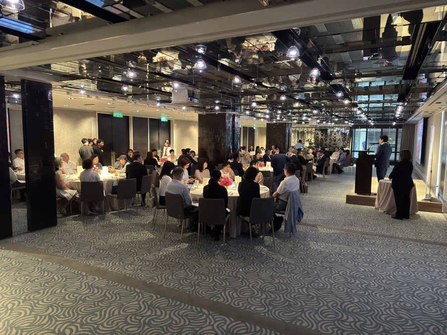 Ballroom session at the second venue, speaker at the lectern, round tables under a mirrored ceiling