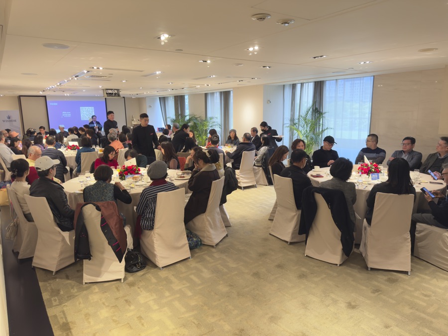 Full roadshow room mid-presentation, speaker at the screen, guests at round tables
